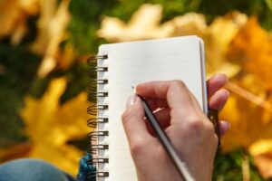 person-writing-in-notebook-with-fall-leaves-behind